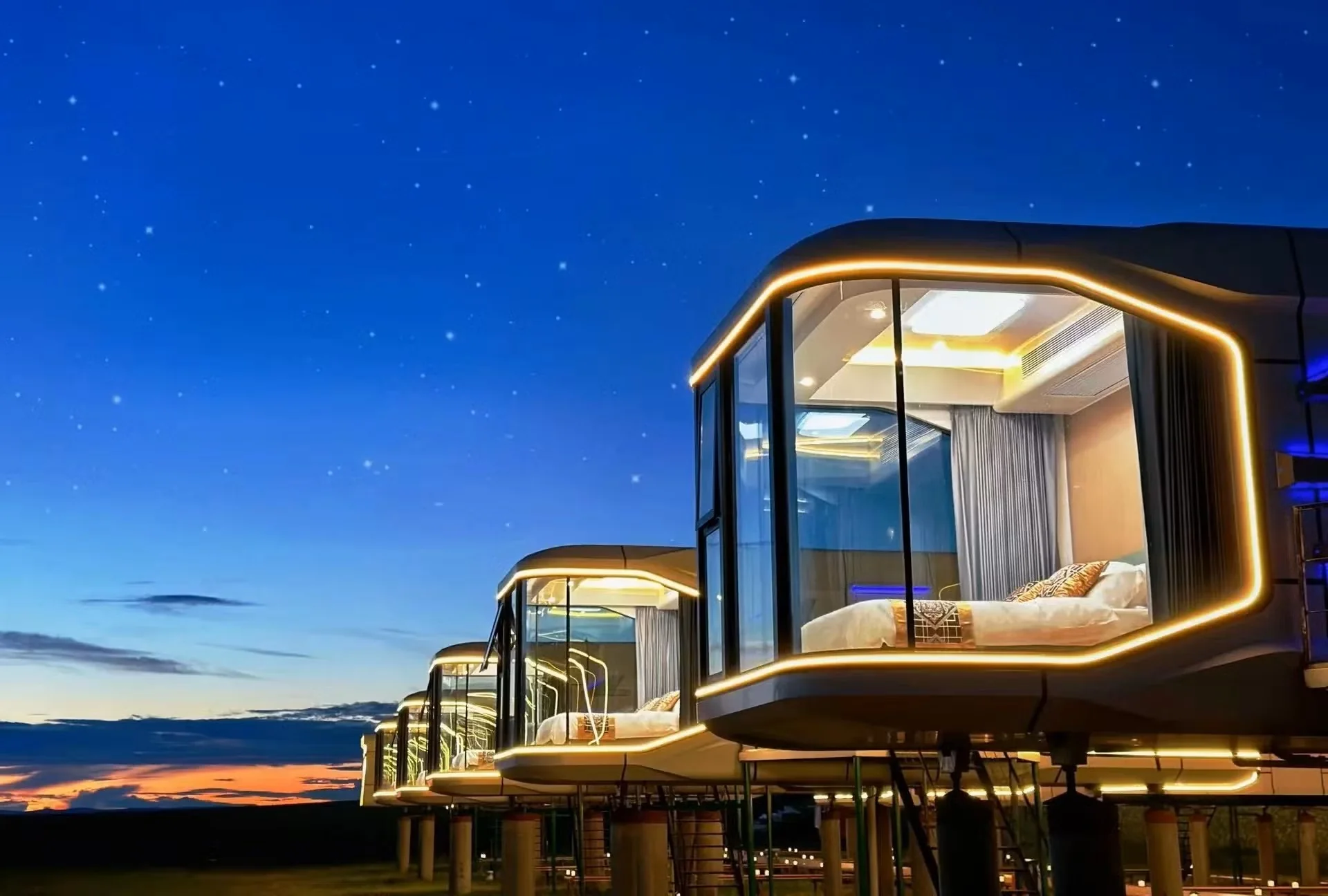 Glass-fronted capsule cabins glowing under a starry night sky