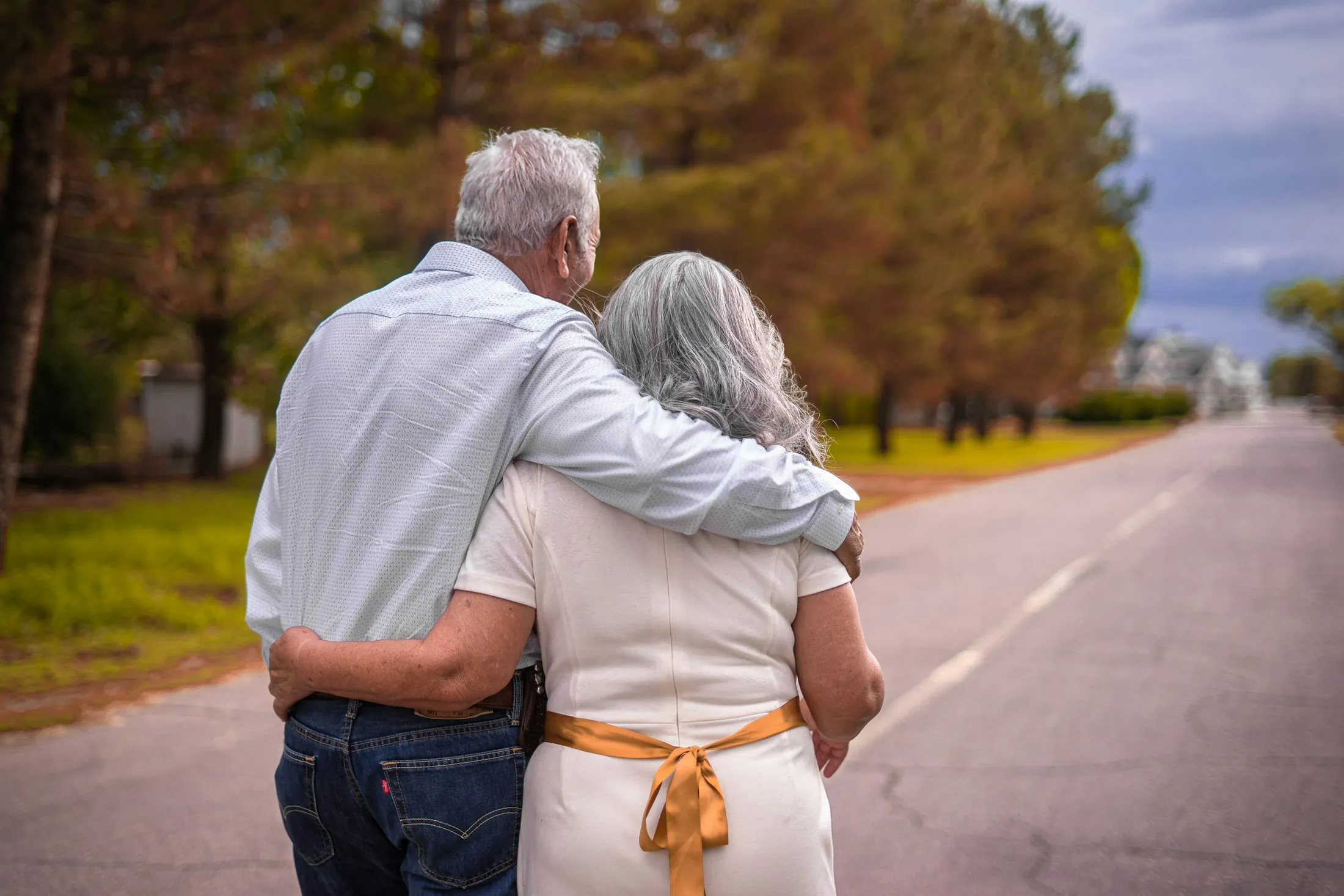 An older couple walking arm in arm along a tree-lined road