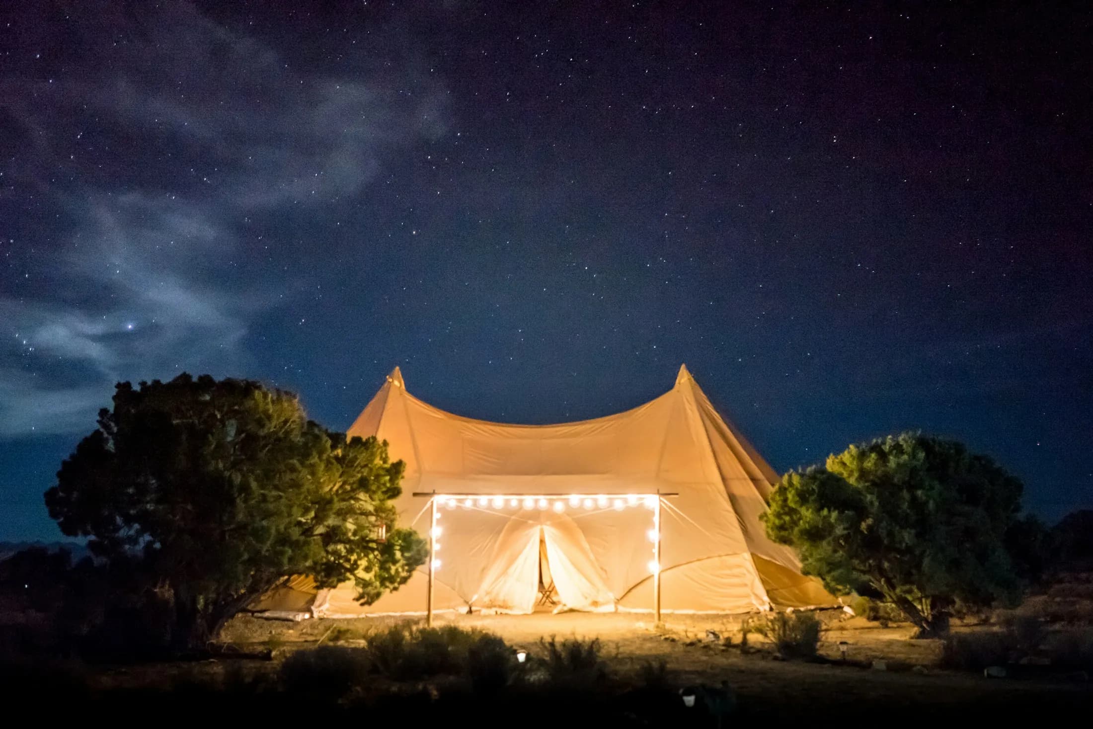 A lit canvas tent under a starry night sky