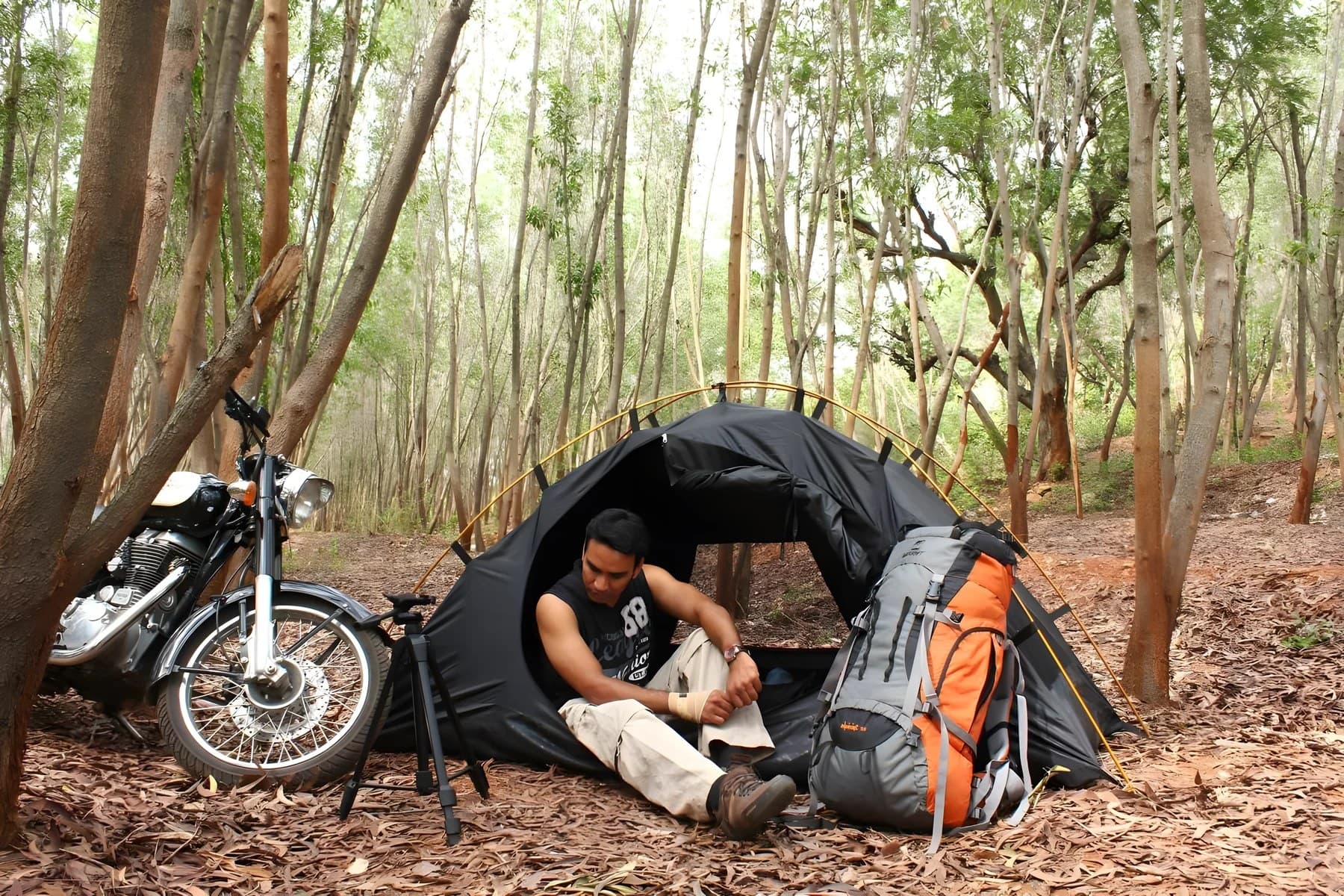 Prakash Natarajan seated at a forest campsite beside his tent and motorcycle